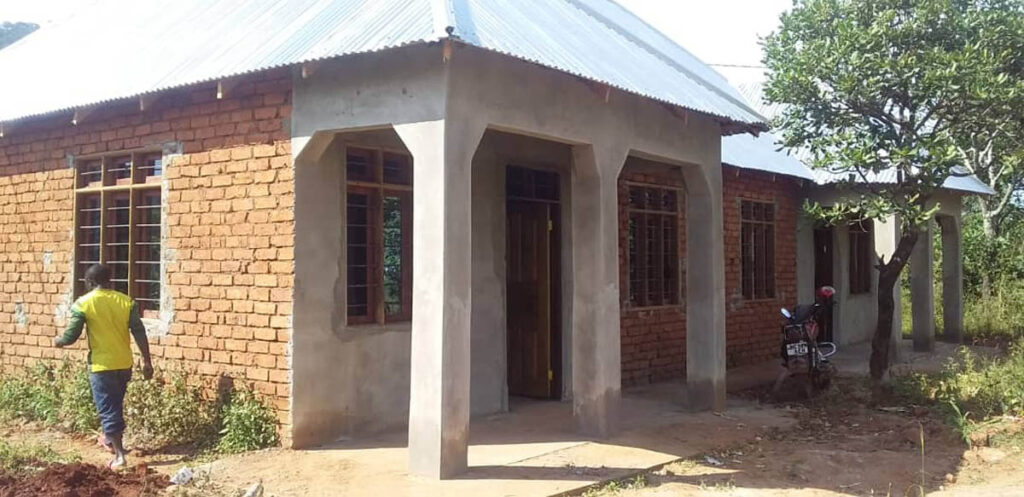 A single-story brick house with a metal roof, glass windows, and a small covered porch; a person and a motorcycle are visible outside.
