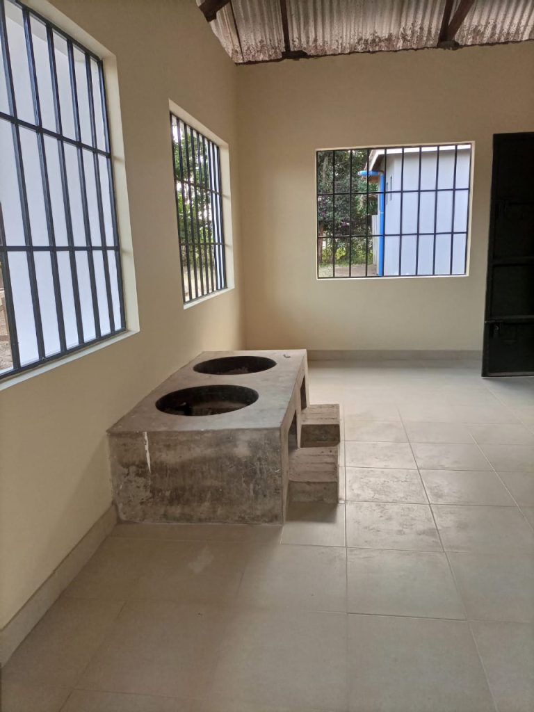 A clean, empty room with tiled floors, barred windows, and a built-in concrete stove with two round openings.