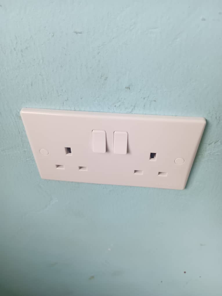 A double electrical wall socket with two switches is installed on a light blue painted wall.