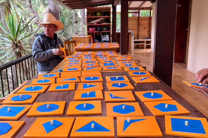 A person in a hat sits at a table covered with orange tiles featuring various blue geometric shapes with white pegs in their centers.