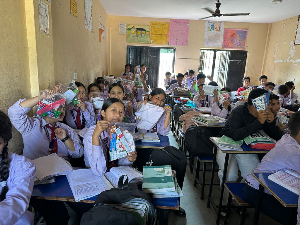 Students in a classroom hold up plastic pouches filled with school supplies.